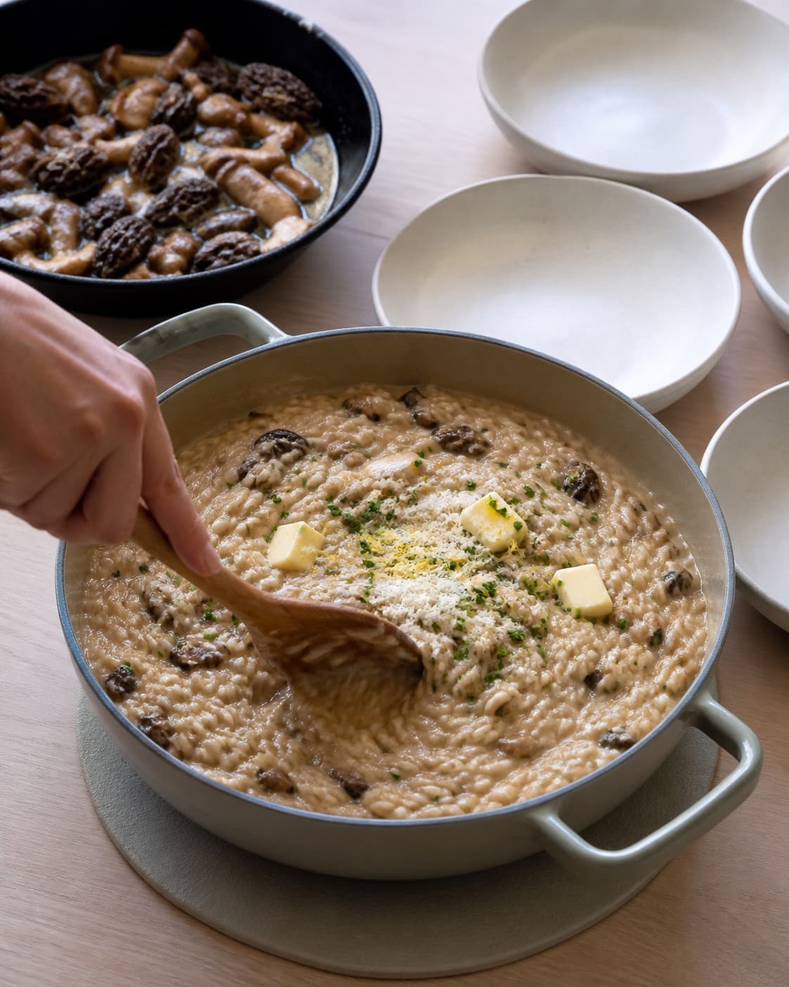 Koldt smør, parmesan, purløg og citronskal røres i den blanke risotto væk fra varmen, mens varme svampe venter i brunet smør