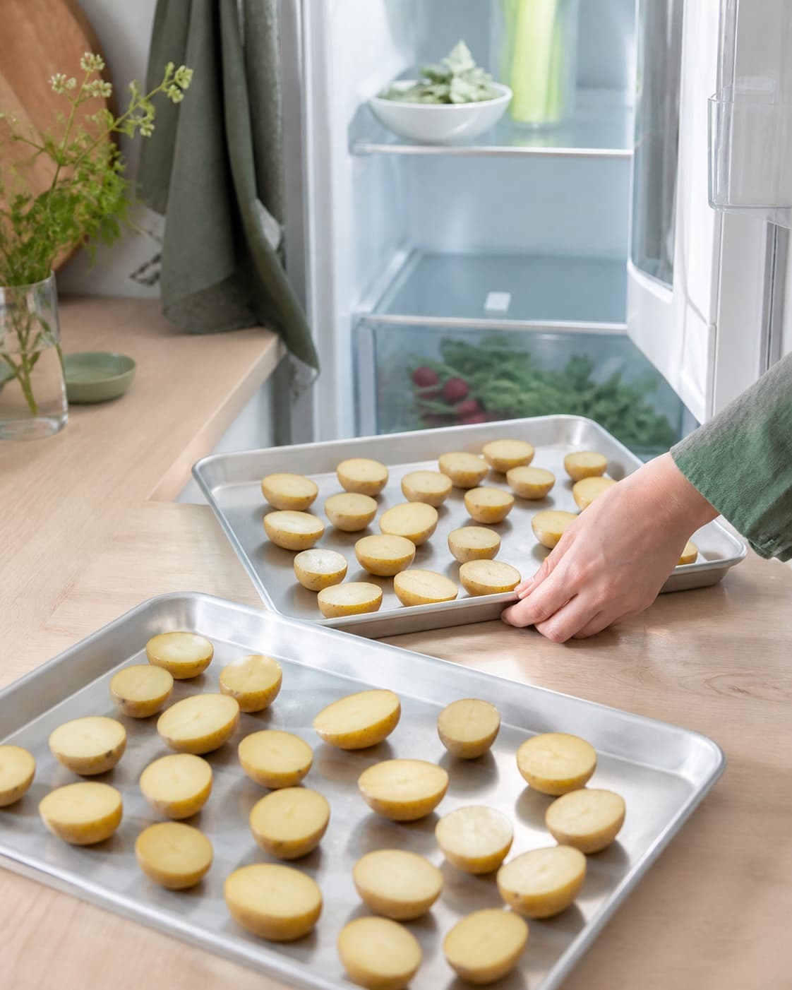 Halve nye kartofler står utildækket i ét lag på to kolde metalbakker, mens den bagerste bakke skubbes ind i køleskabet