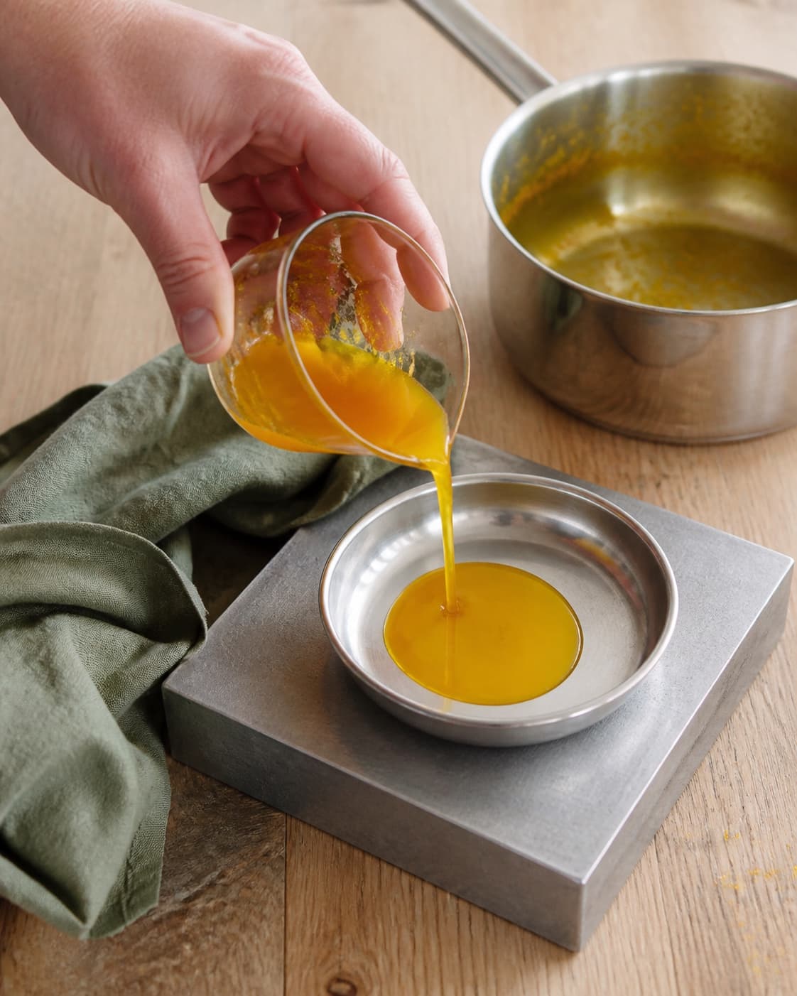 En lille portion blank koncentreret appelsinsirup hældes fra målebæger i en lav stålskål på køleblok ved den næsten tomme gryde