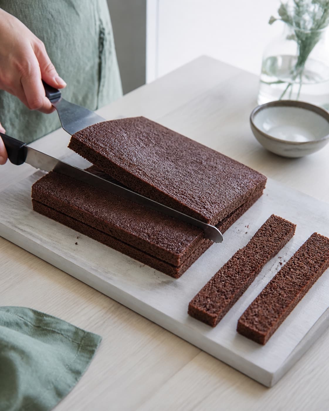 En lang savtakket kniv deler den helt kolde chokoladekage vandret, mens en bred kageløfter støtter det øverste lige lag