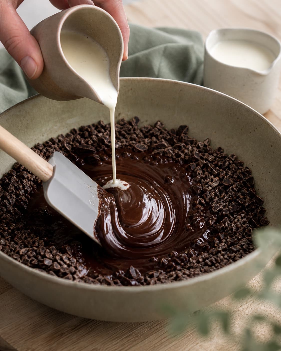 Første portion varm fløde hældes i midten af hakket mørk chokolade, mens en dejskraber samler en blank emulsion indefra