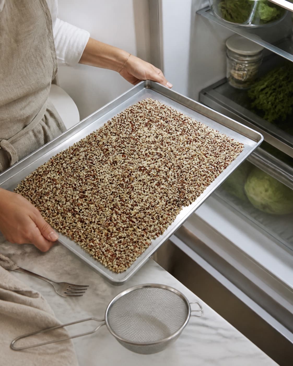 Kogt trefarvet quinoa med frigjorte spiraler er bredt i et tyndt tørt lag på en ren metalplade på vej ind i køleskabet