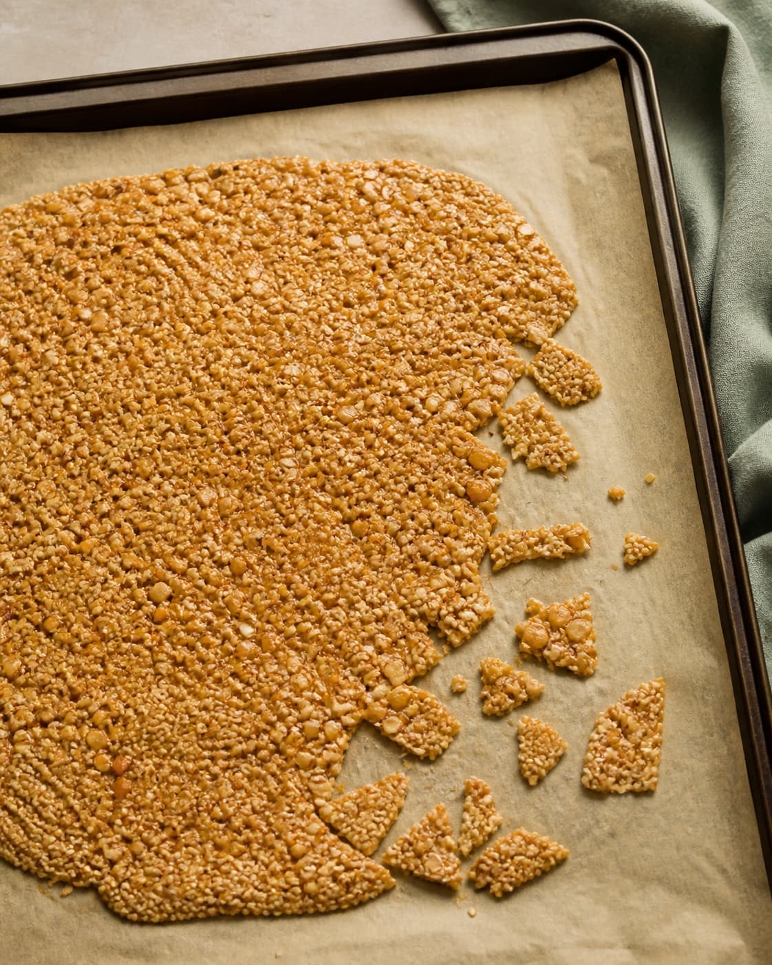 Tyndt gyldent peanut-sesamknas køler helt på bagepapiret og brækkes derefter i små tørre flager uden mørke kanter