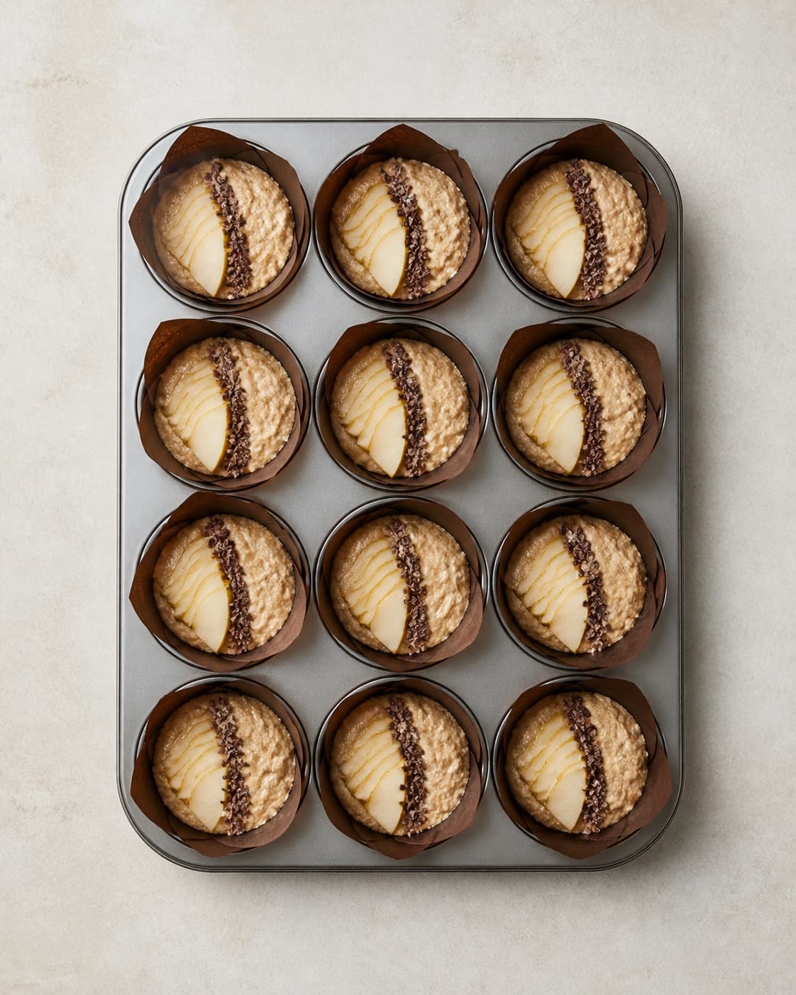 Præcis tolv rå muffins står ens fyldt i tre kolonner med fire og har hver en tynd pærevifte samt én smal linje kakaonibs