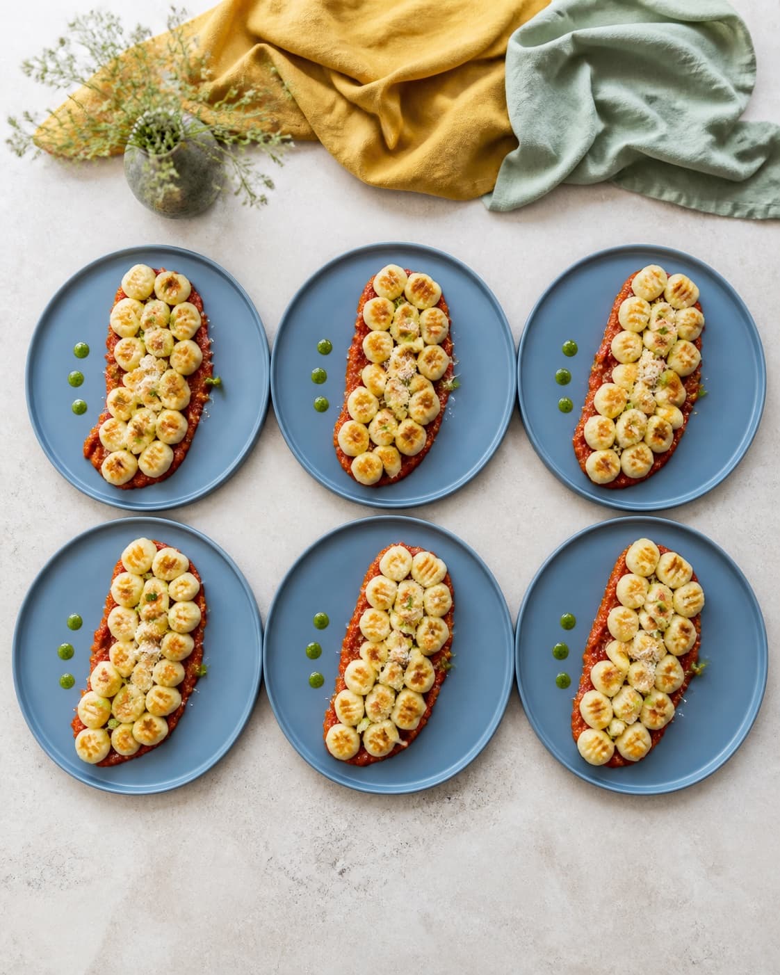 Præcis seks støvet blå tallerkener har hver en generøs hovedretportion riflede gnocchi med én gylden side over rød sauce og tre grønne oliedråber