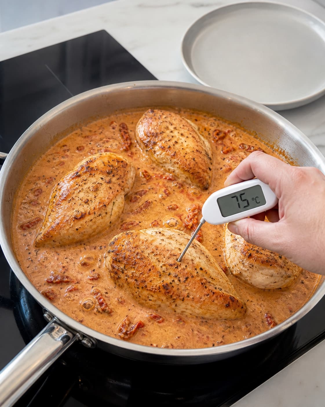 Præcis fire gyldne kyllingebryster simrer roligt i soltomatsauce, mens den tykkeste midte måles til 75 °C med et rent termometer