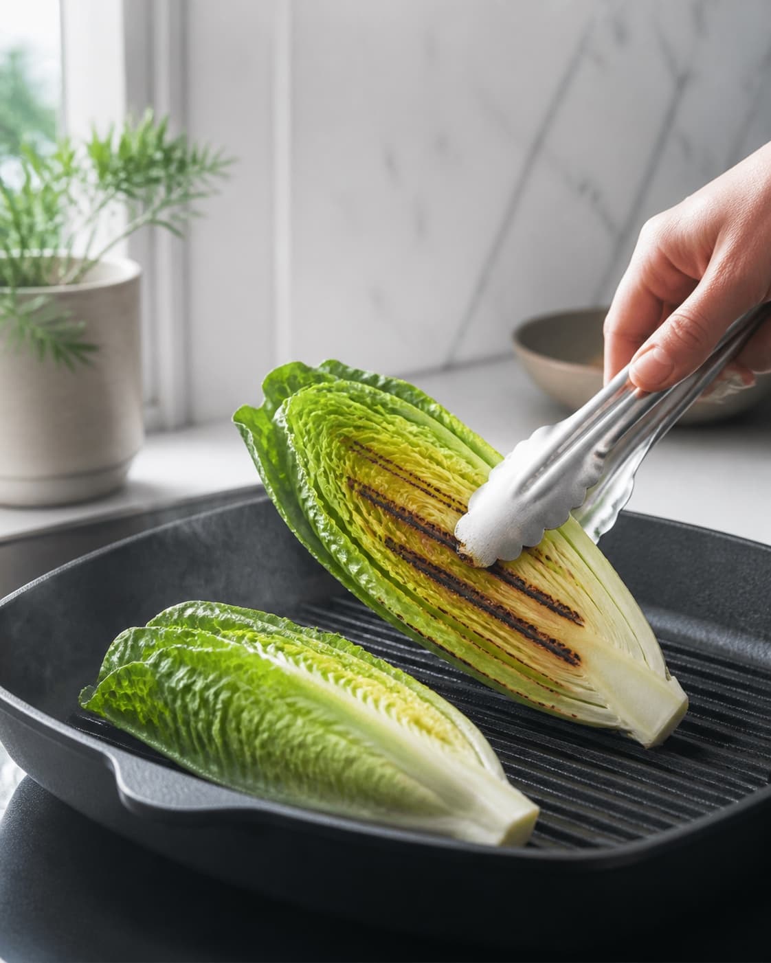 To tørre romainehalvdele får kort hård kontakt på grillpanden, og én løftes med tydelige mørke striber samt fast grøn sprød kerne