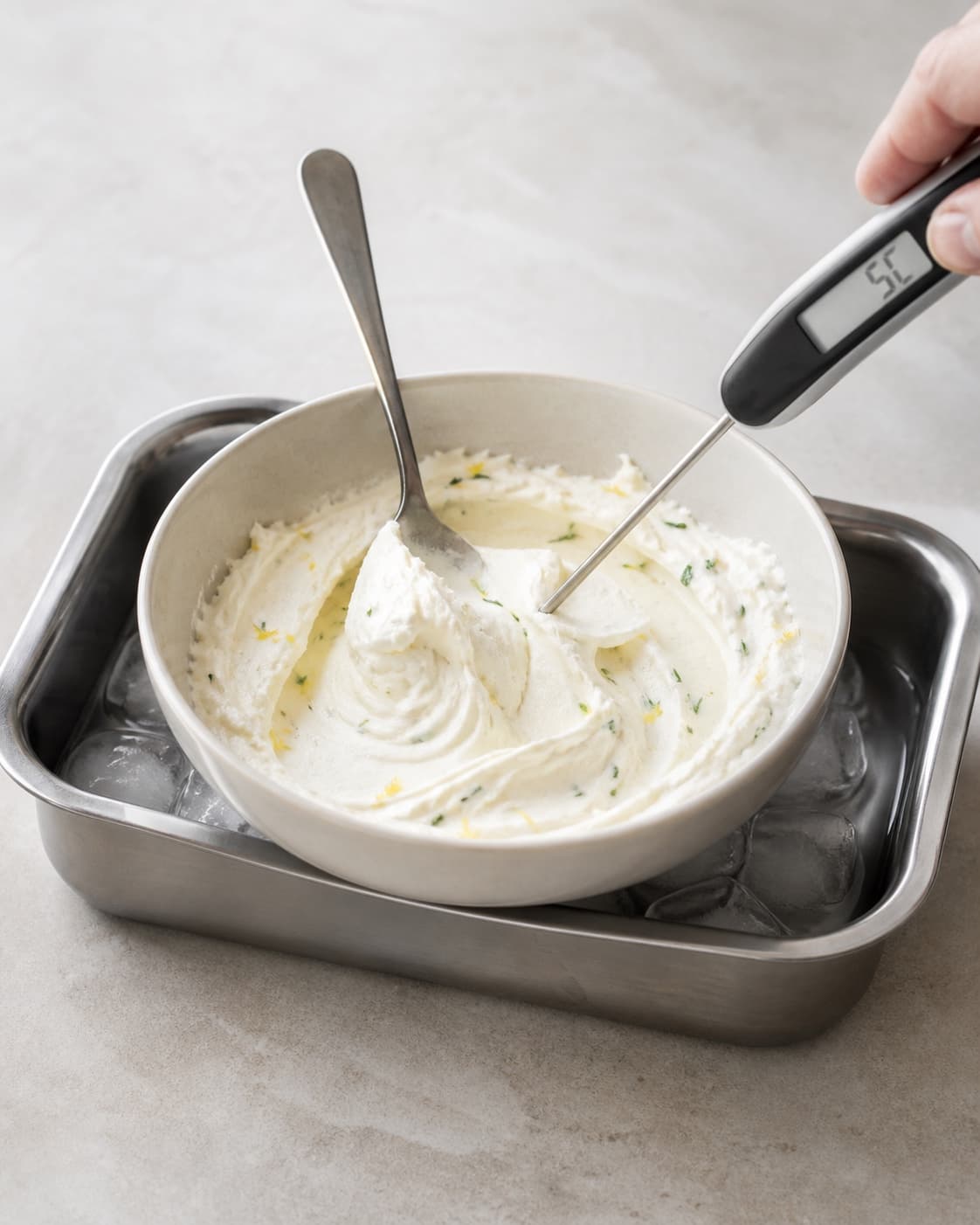 Fast glat gedeostcreme med citron og fine rosmarinprikker holder en tydelig ske-top i et isbad og måles til 5 °C uden væskekant