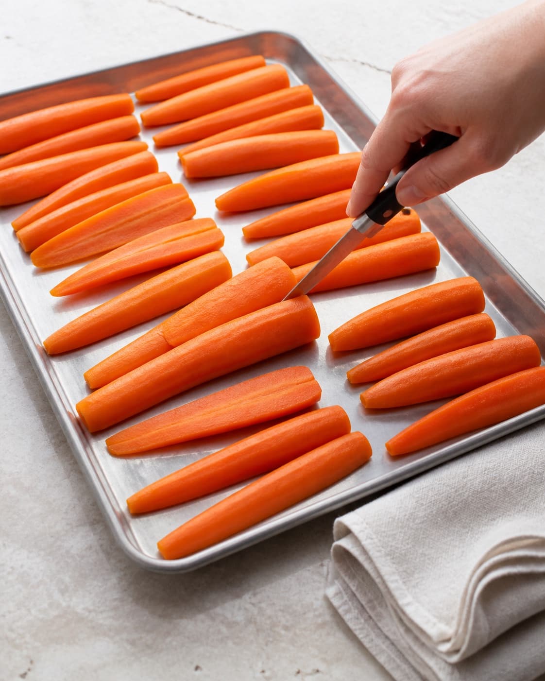 Ens tykke fortilberedte gulerodsspid ligger matte og helt tørre på metalbakke, mens en lille kniv prøver den faste orange midte