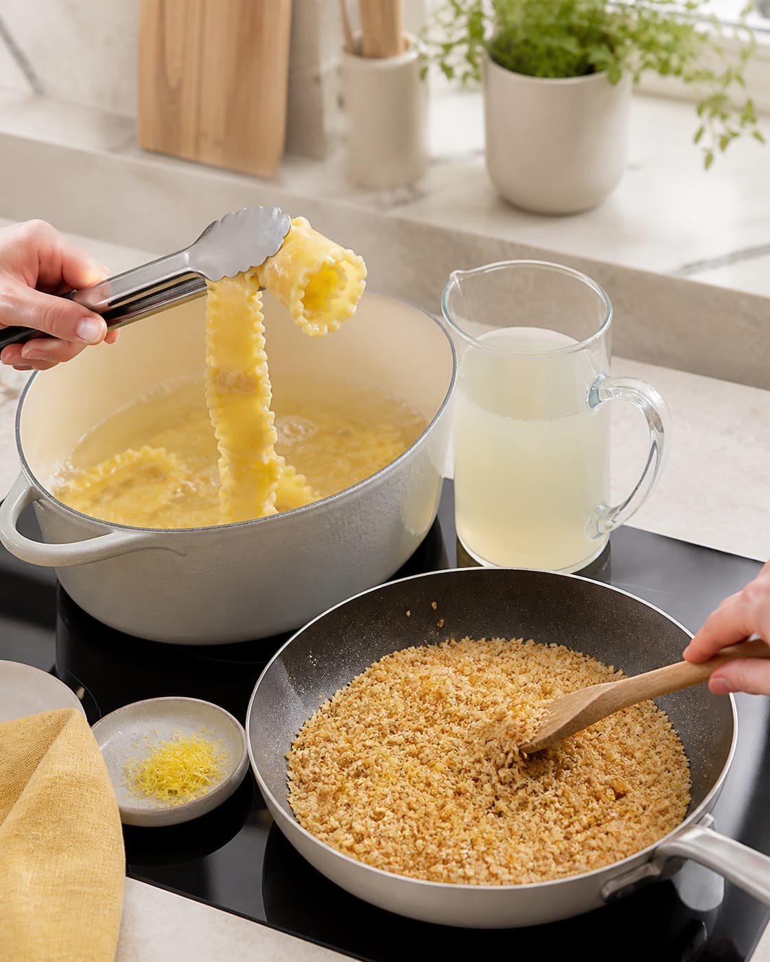 Brede riflede mafaldinebånd løftes al dente fra gryden ved siden af gemt pastavand og en pande med tør ensartet gylden citronpanko
