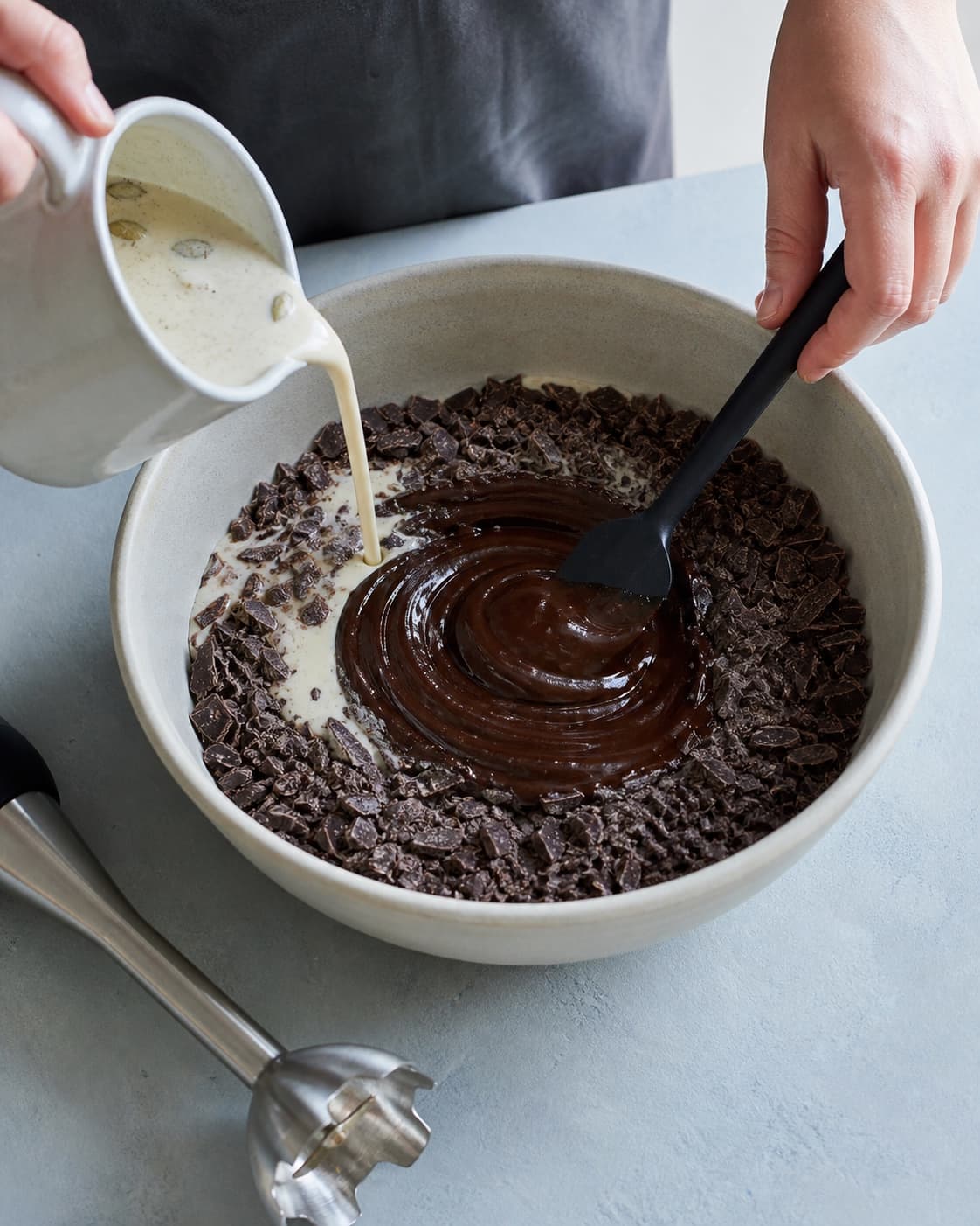 Første tredjedel varm infuseret fløde hældes over chokoladen, mens en blank mørk emulsion røres frem fra midten