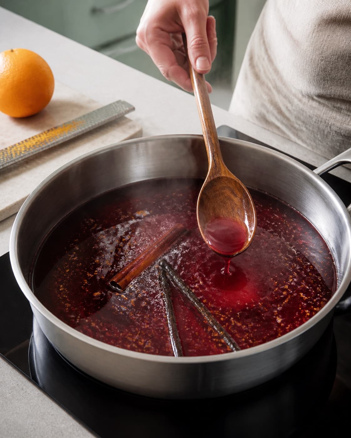 Klar mørkerød kirsebær-solbærbase simrer med appelsinskal, flækket vanilje og kanel, mens sukkeret røres helt ud