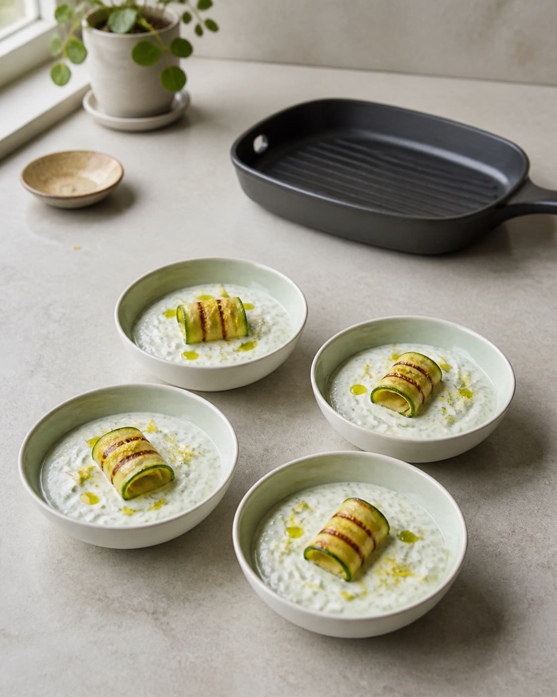 Fire kolde skåle tæt squashtzatziki har hver ét løst rullet squashbånd med fine brune grillstriber, citron og få oliedråber