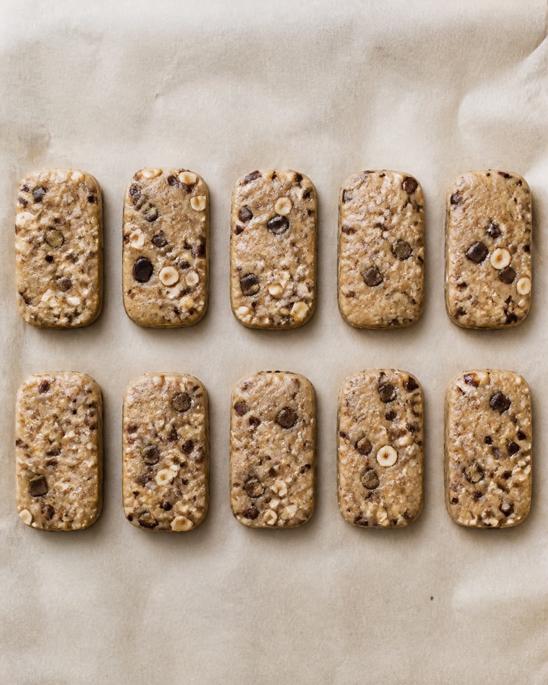 Præcis ti rå afrundede cookiebarer ligger i to rækker med jævnt fordelte chokoladestykker og hasselnødder