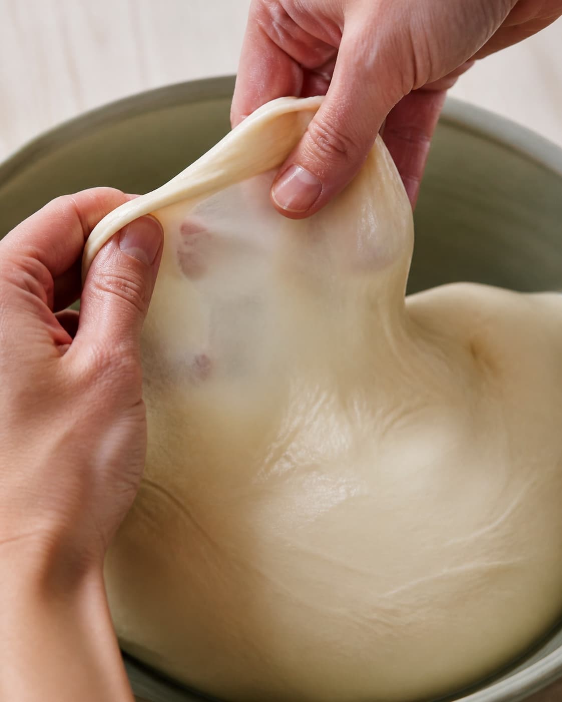 Blank elastisk pizzadej strækkes mellem fugtige fingre til et tyndt næsten gennemsigtigt glutenvindue uden rivning