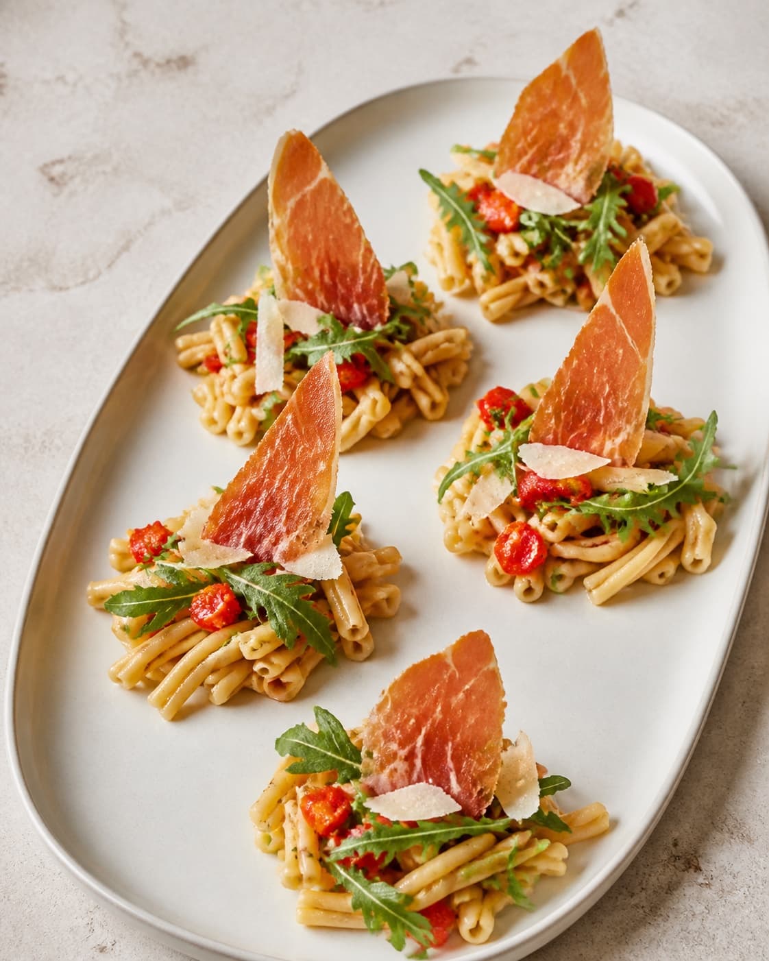 Præcis fem adskilte portioner kort pasta toppes hver med peberfrugt, rucola, parmesan og ét sprødt skinkesejl
