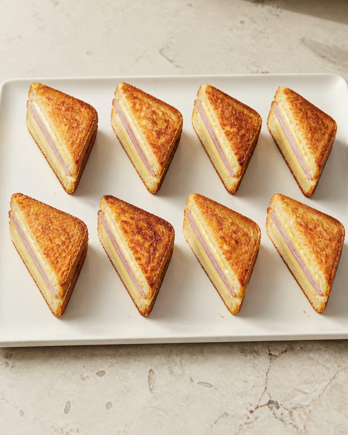Præcis otte croque monsieur-trekanter står i to rækker med sprødt brød og lige lag af skinke og ost
