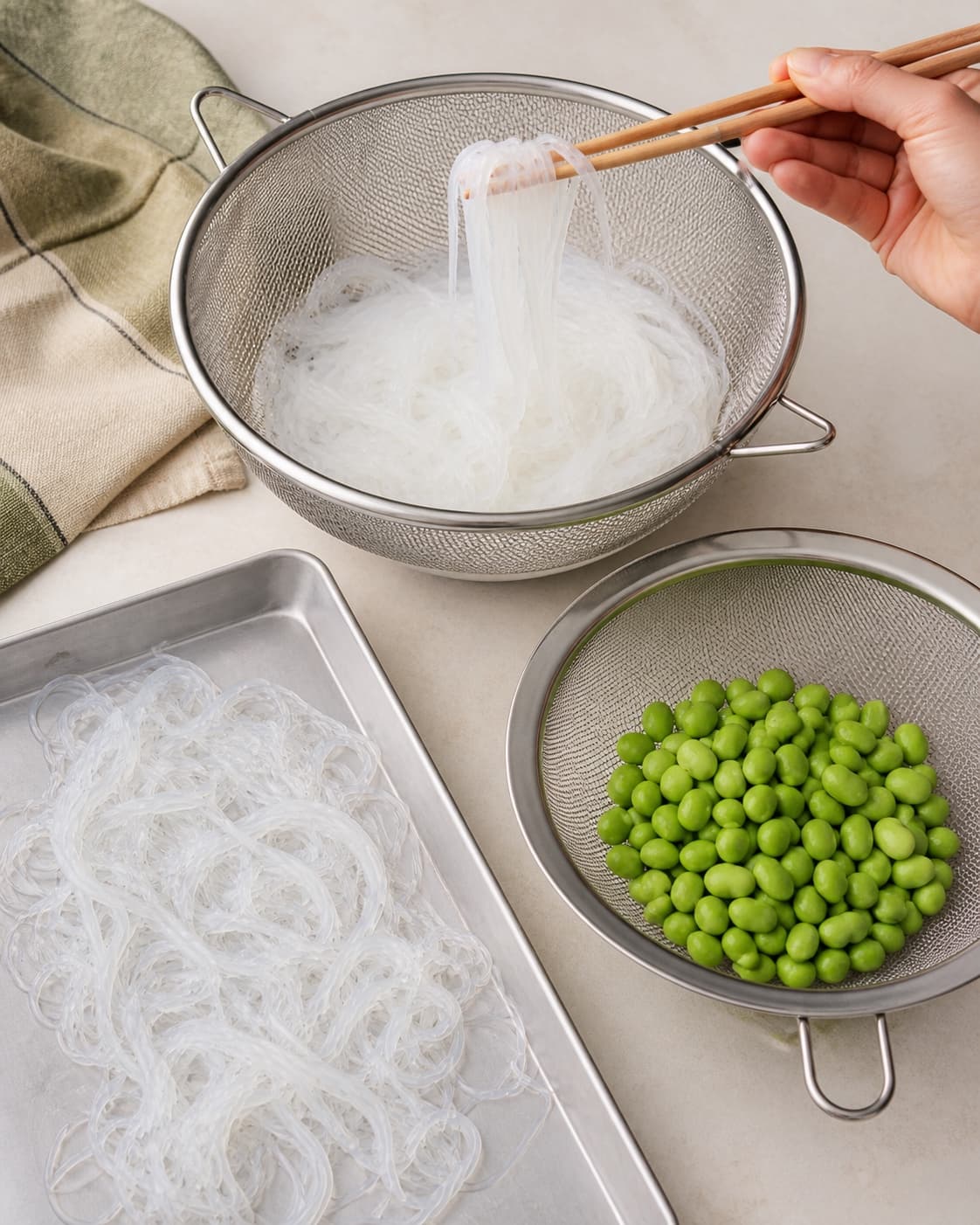 Transparente glasnudler drænes og løftes løse med pinde ved siden af separat afdryppede grønne edamame