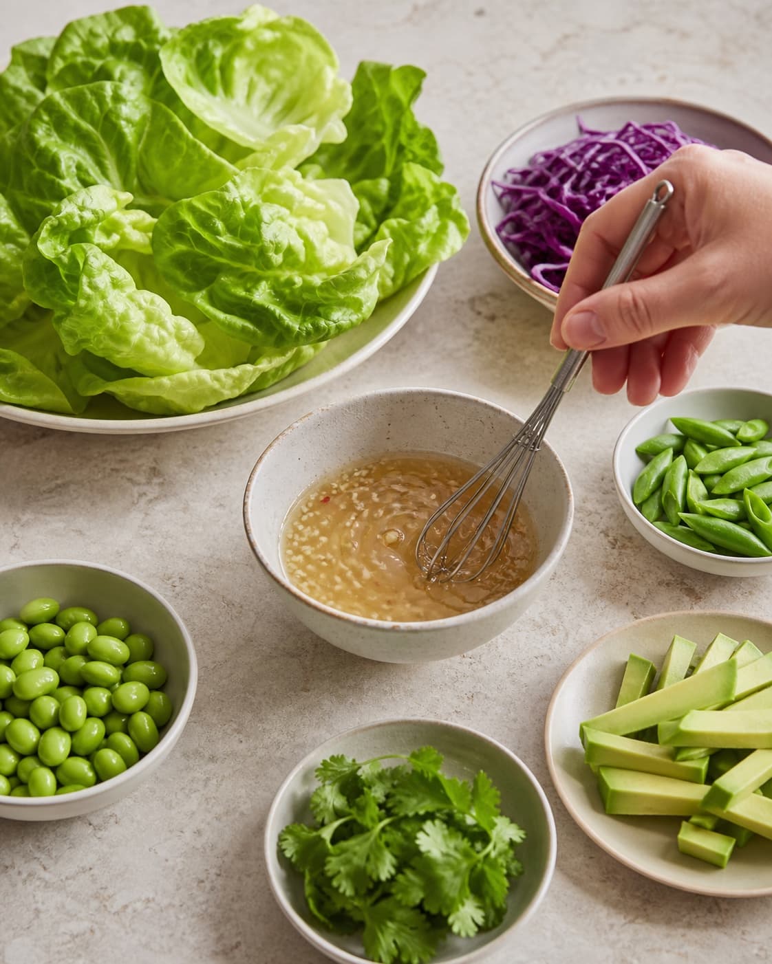 Tørre salatblade, rødkål, sukkerærter, avocado og edamame står klar, mens lime-ingefærdressing piskes