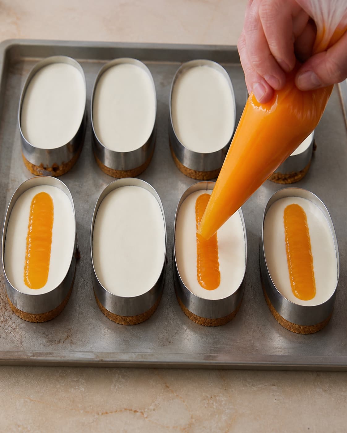 En smal orange curdribbon sprøjtes midt i otte ovale forme mellem to rene hvide cremelag