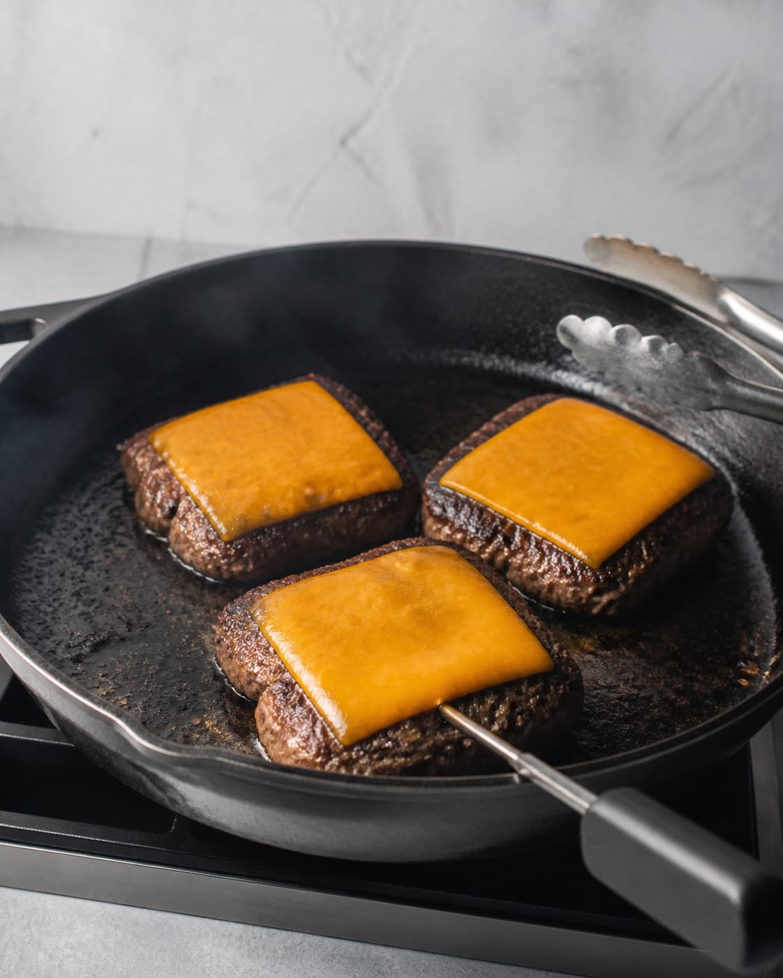 Tre firkantede gennemstegte oksebøffer har smeltet cheddar, mens et termometer måler den forreste