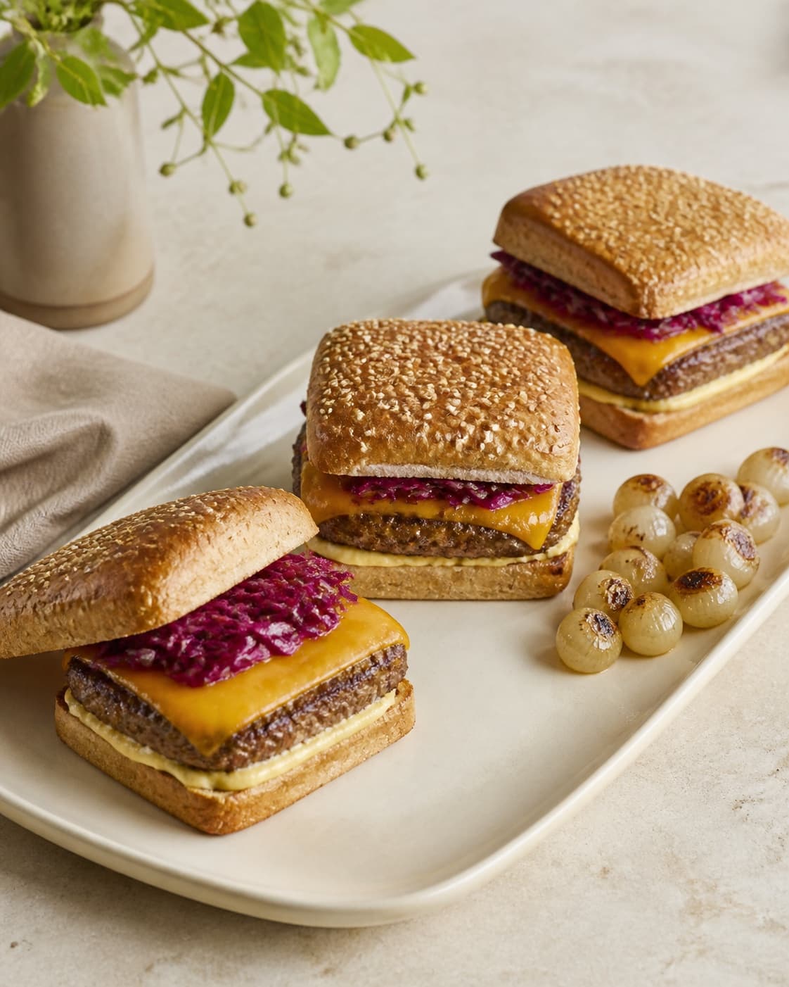 Præcis tre lave firkantede cheeseburgere viser tør sesambolle, brun bøf, cheddar og afdryppet rødkål
