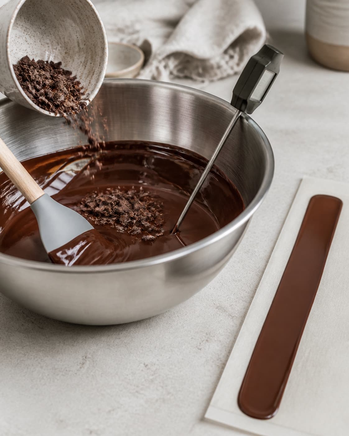Finthakket mørk chokolade tilsættes den blanke masse under omrøring ved siden af en ensartet prøvestribe