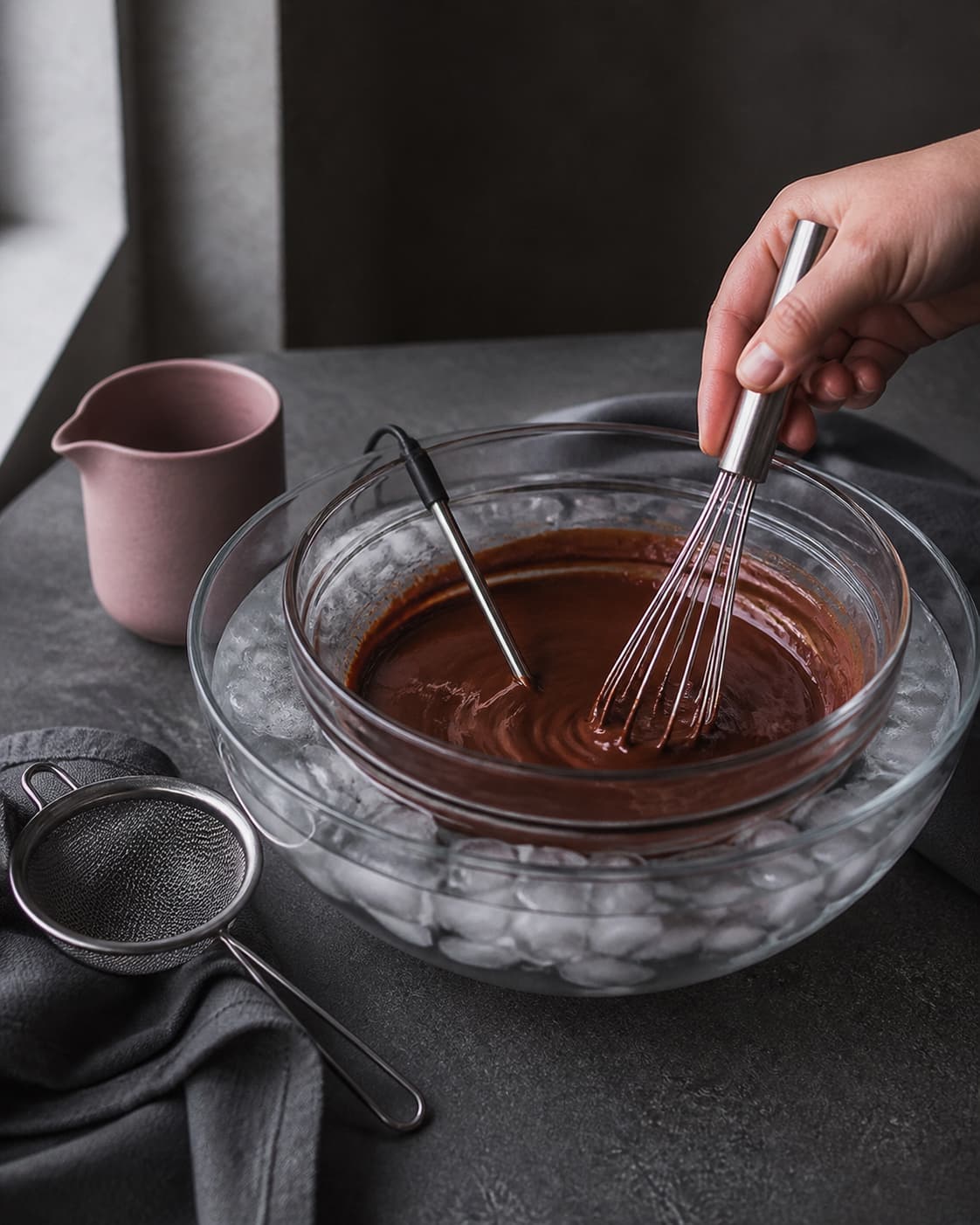 Blank chokoladecreme røres i skål over isbad med piskeris og termometer