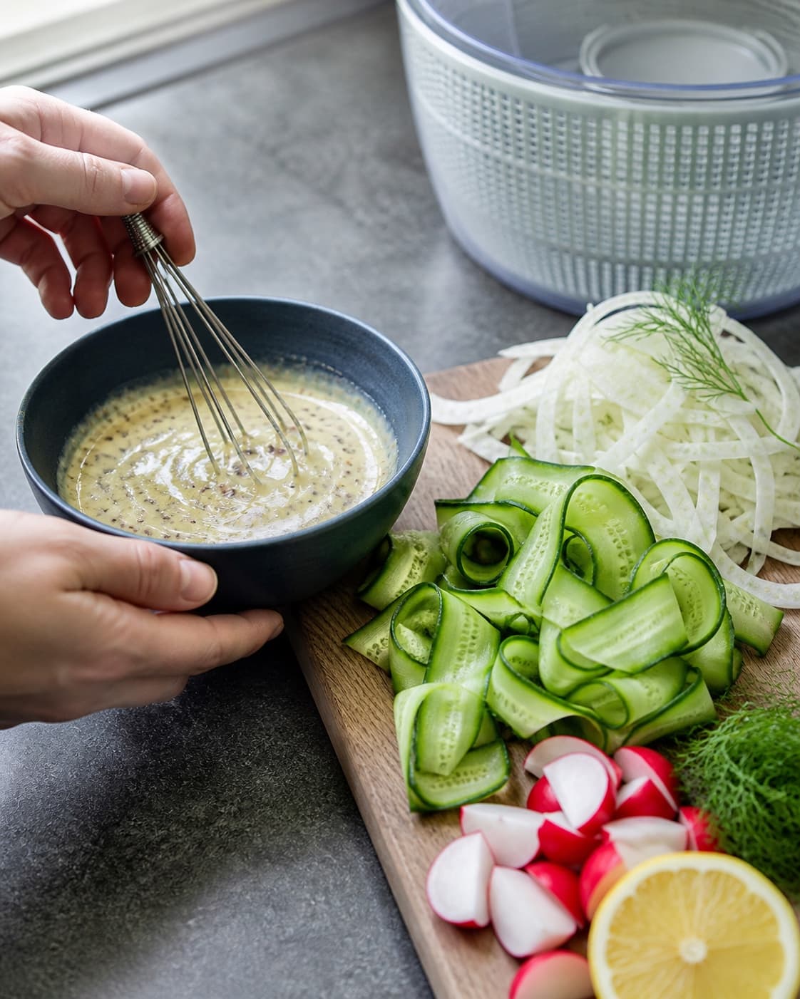 Kold citron-sennepsdressing piskes ved siden af tør fennikel, agurkebånd, radisekvarte og dild på rent bræt