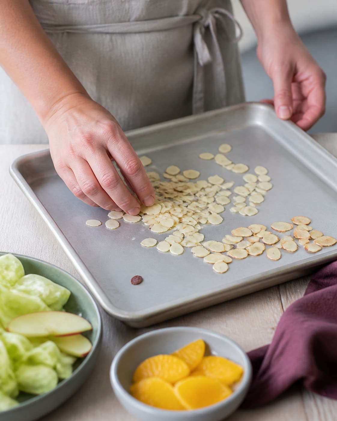 Mandelflager fordeles på en lys bageplade med let gyldne flager samlet for sig og ét mørkt stykke frasorteret
