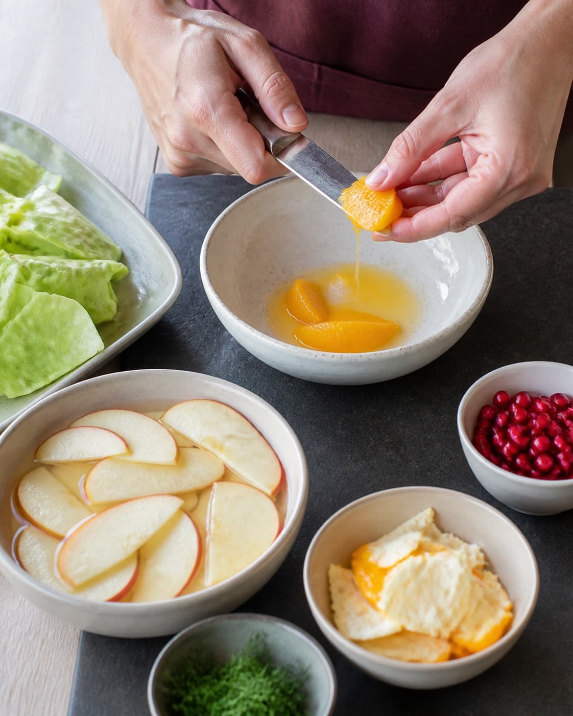 Appelsin fileteres over en skål med saft, mens tynde æbleskiver, granatæblekerner og hakket dild holdes adskilt