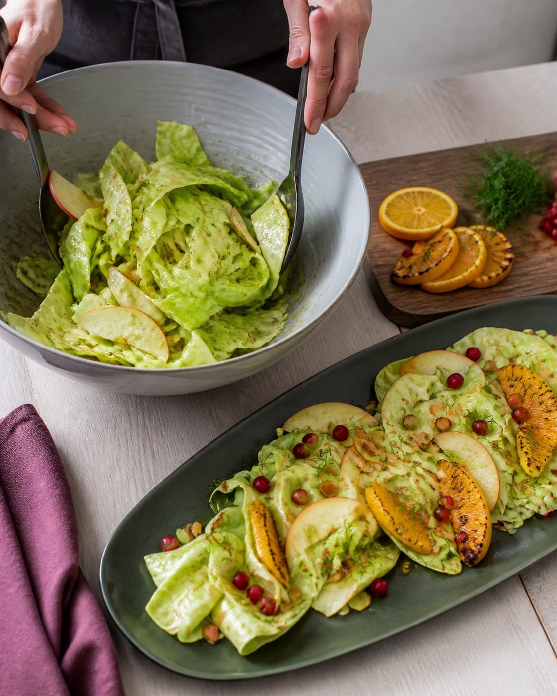 Spidskålsbånd og æble vendes let med dressing, mens salaten anrettes luftigt med appelsin, granatæble og dild