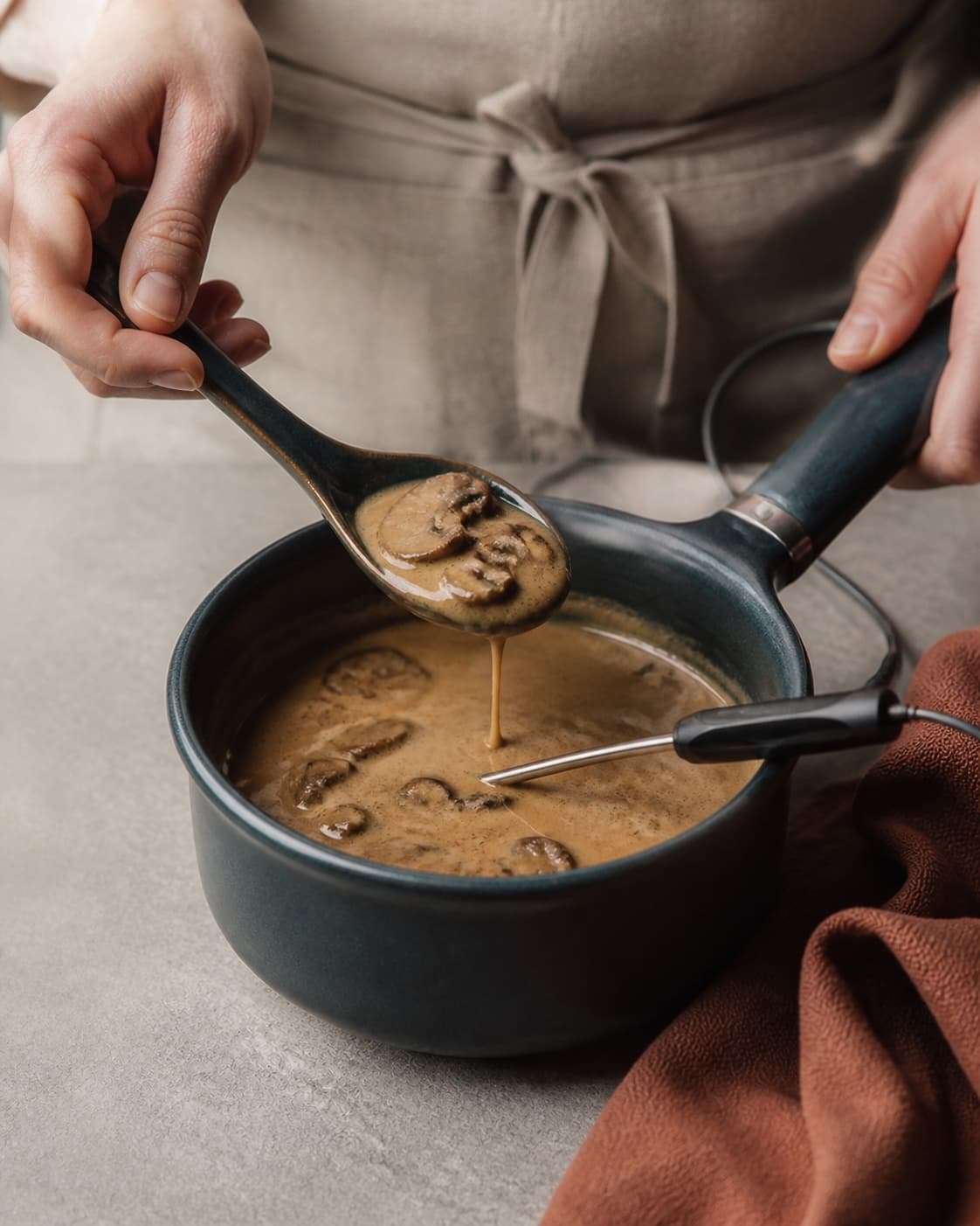Blank champignonsauce med tydelige svampeskiver dækker en løftet ske, mens centrum måles med digitalt termometer