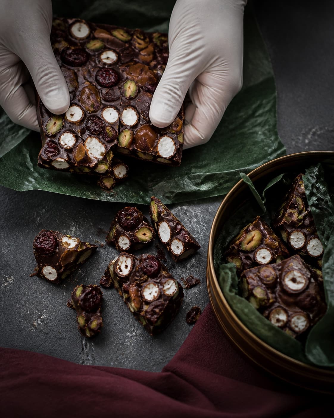 Tørre behandskede hænder brækker en fast rocky road-plade i stykker, som pakkes i bronzefarvet dåse med papir imellem