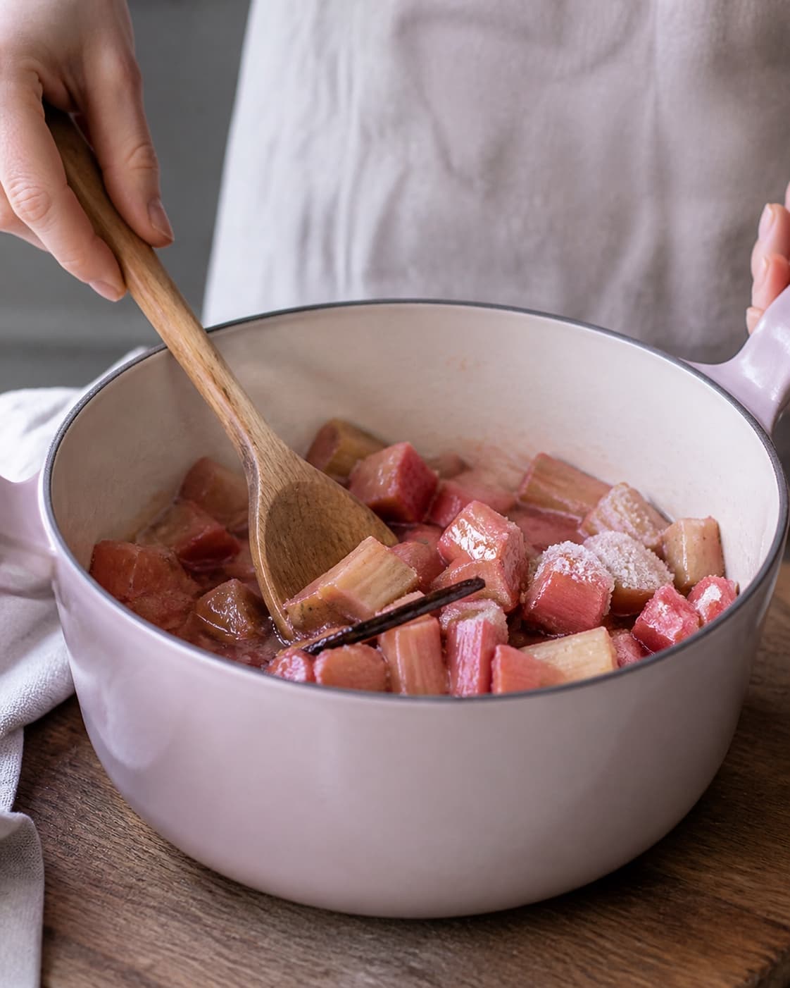 Rå rabarberstykker vendes med sukker, hyldeblomstsaft, citron og vaniljestang i en bred lyserød gryde