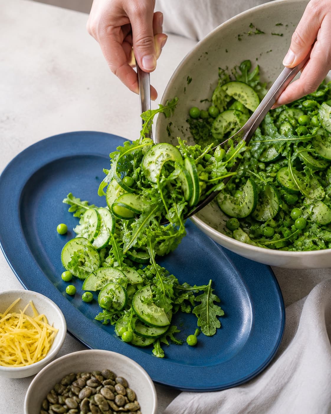 Agurk, tør rucola, kolde ærter og dild vendes let og flyttes luftigt til koboltblåt fad med kerner og citron separat