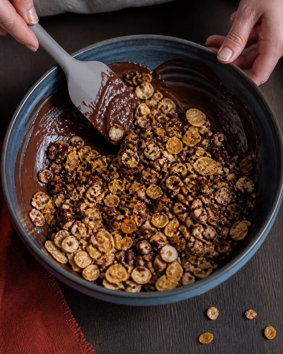 Hele cornflakes, afkølede hasselnødder og appelsintern løftes kort gennem blank chokolade med bred spatel