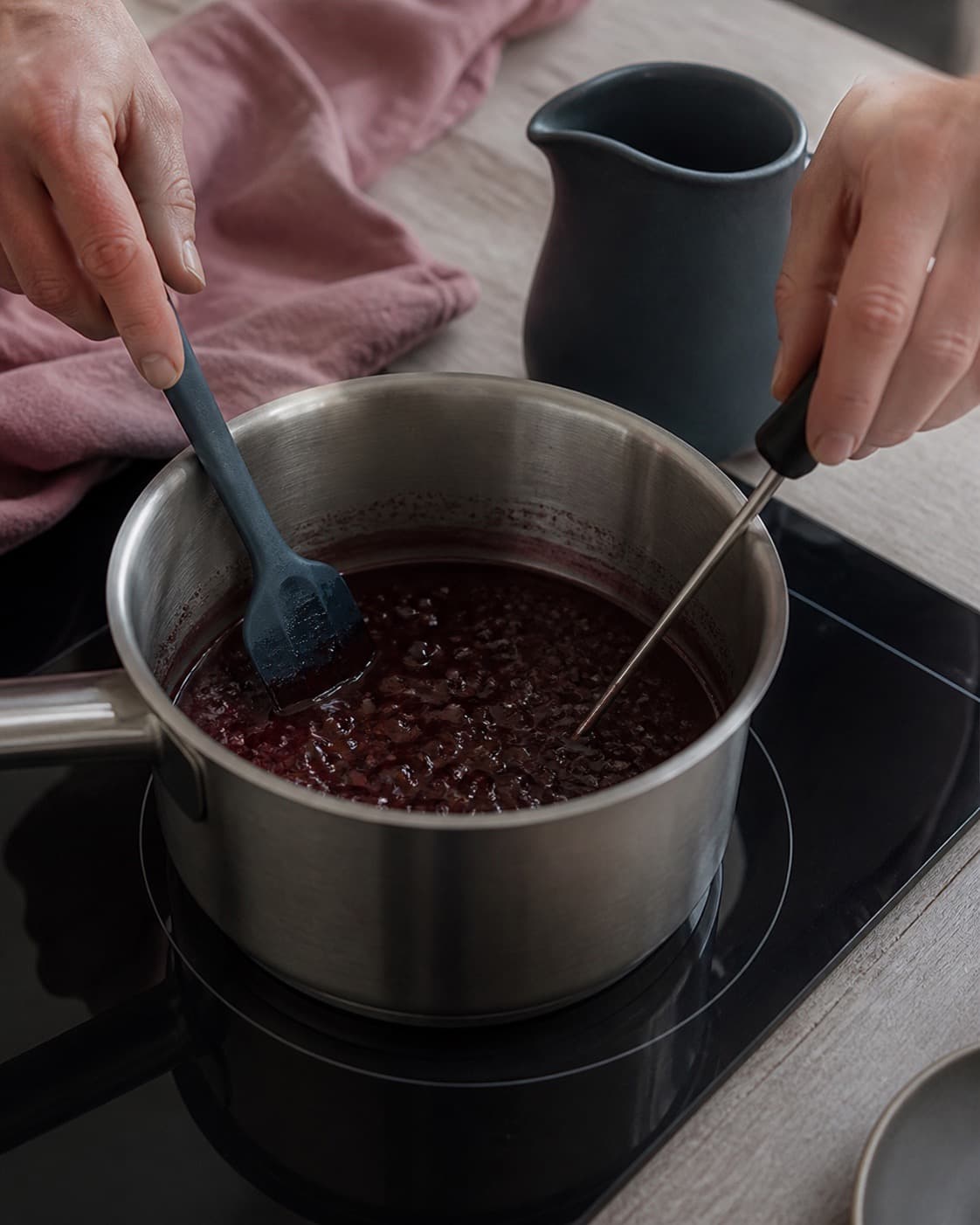 To hænder rører og måler en roligt boblende granatrød reduktion med termometerdisplayet vendt væk fra kameraet