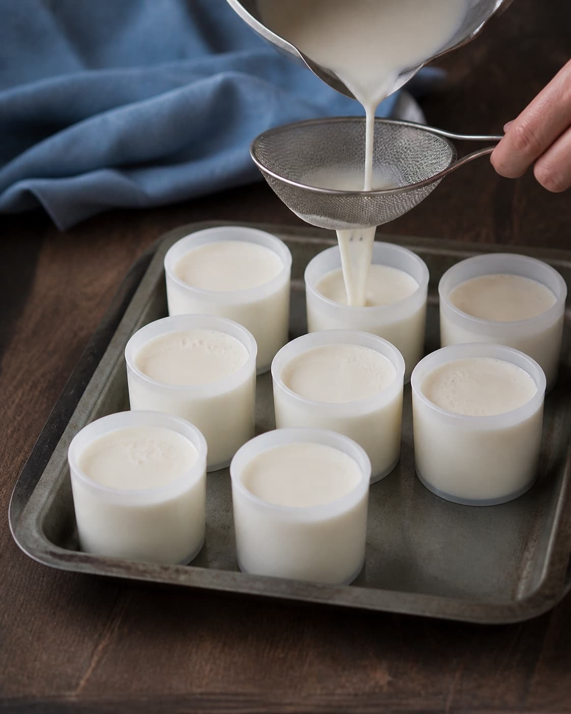To hænder fylder ens små silikonecylinderforme med blank panna cotta gennem en fin sigte på en kold bakke