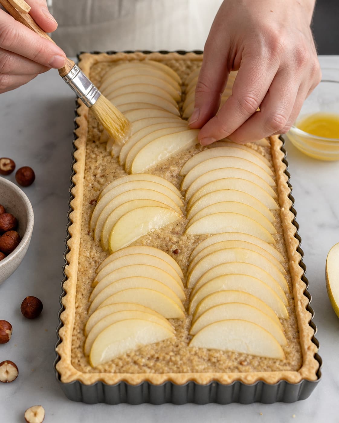 Pærevifter lægges i ens rækker over hasselnøddefrangipane i rektangulær bund