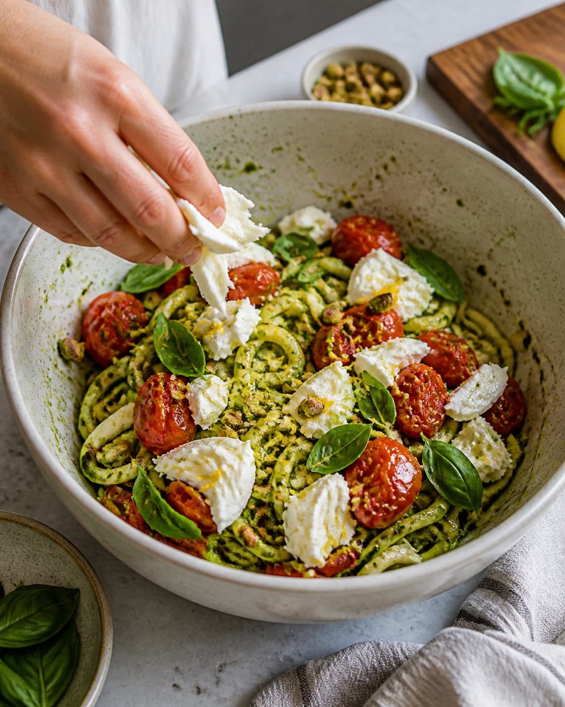Bagte tomater og store burratastykker lægges på pesto-coatede squashspaghetti