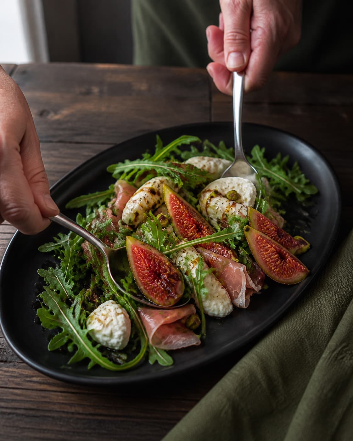 figensalaten vendes nænsomt med citron-balsamicodressingen under tilberedningen af figensalat med burrata, parmaskinke og pistacie