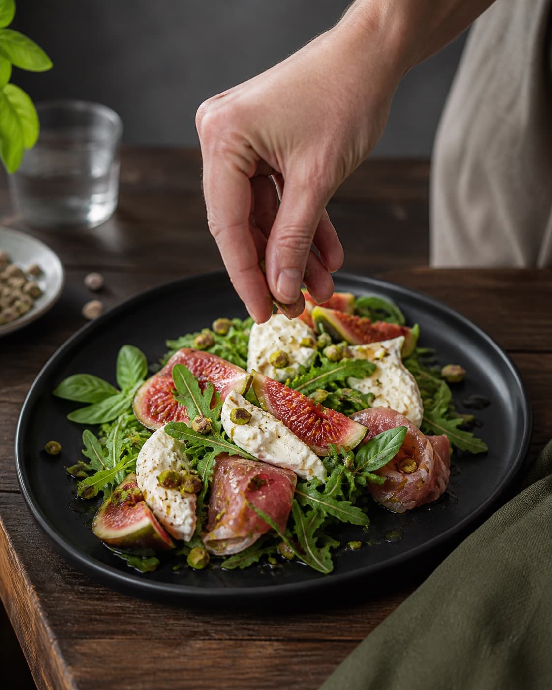 figensalaten anrettes luftigt med burrata, pistacie og basilikum under tilberedningen af figensalat med burrata, parmaskinke og pistacie