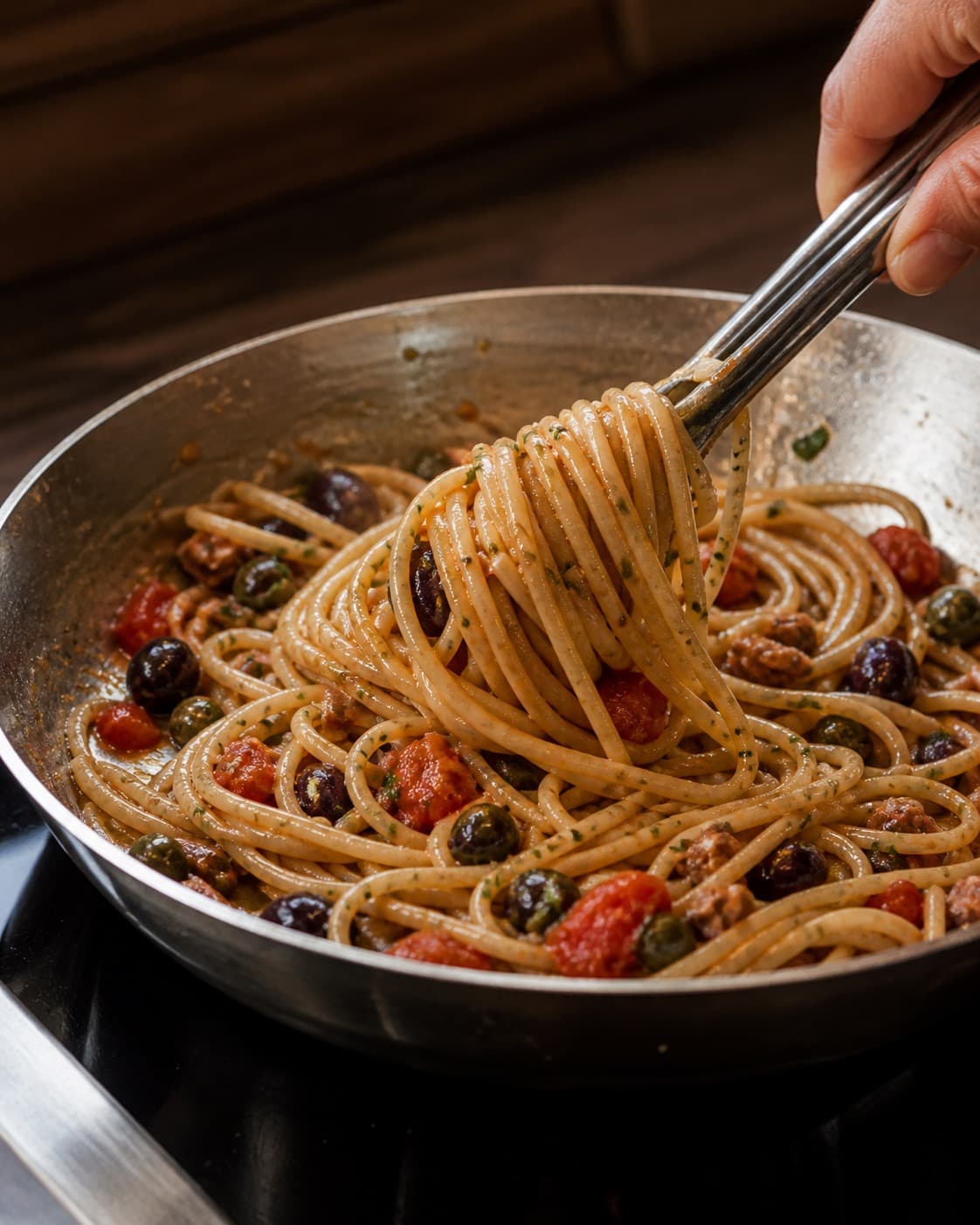 Pasta svinges blank med ovntomat, oliven, ansjos og kapers og en smule pastavand under tilberedningen af spaghetti puttanesca med ovntomat og sprøde kapers