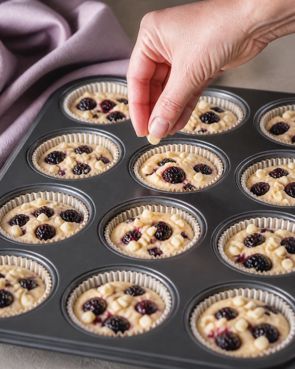 brombær og hvid chokolade fordeles jævnt i den ubagte brombærmuffinsene under tilberedningen af brombærmuffins med citron, hvid chokolade og crumble