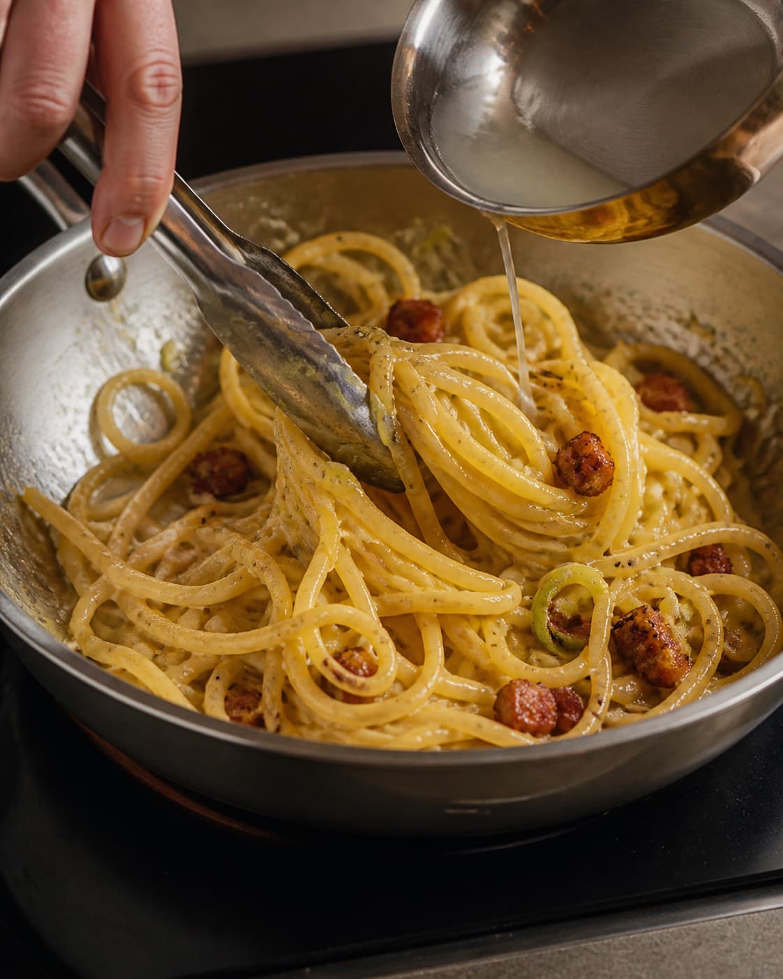 Pasta svinges blank med guanciale, porre og peberfedt og en smule pastavand under tilberedningen af spaghetti carbonara med porre og sprød guanciale