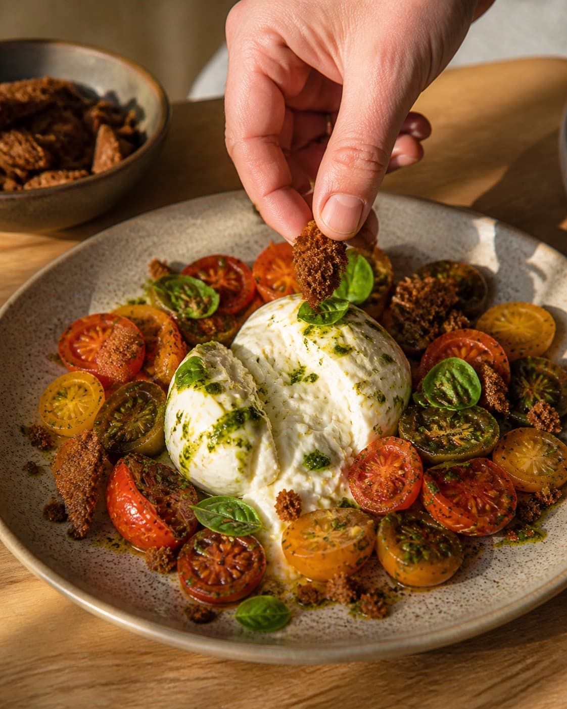 burrata med tomater anrettes luftigt med burrata og sprøde rugbrødschips under tilberedningen af burrata med tomater, urteolie og sprødt rugbrød