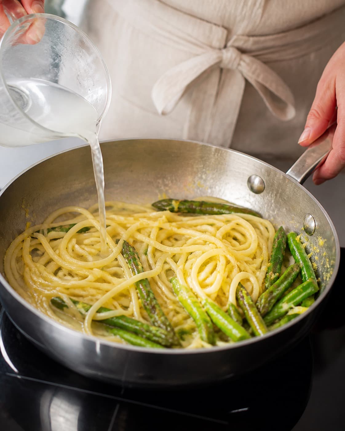 Pasta svinges blank med asparges, citron og smør og en smule pastavand under tilberedningen af citronpasta med asparges, mynte og pecorino