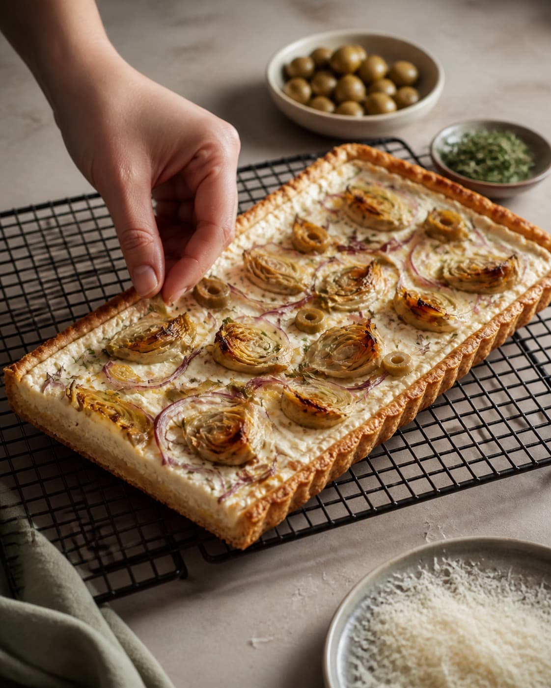 artiskoktærten hviler på rist før oliven, timian og parmesan tilføjes under tilberedningen af artiskoktærte med ricotta, citron og oliven