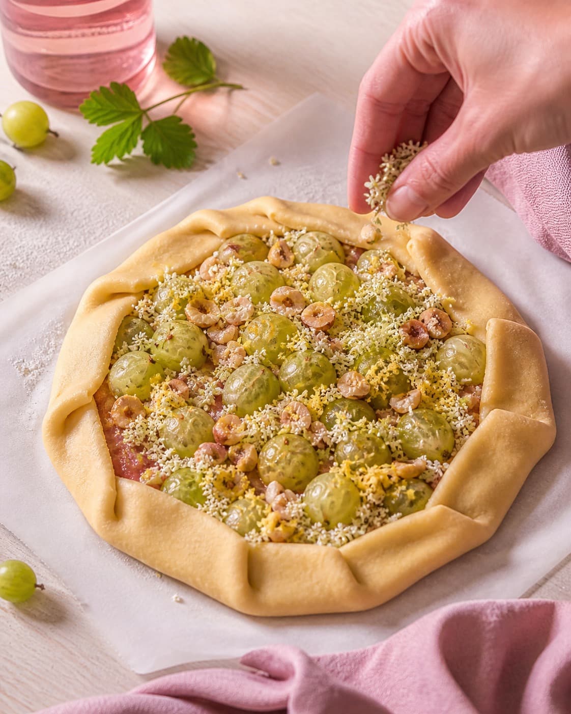 stikkelsbær, hyldeblomst og citron fordeles jævnt i den ubagte stikkelsbærgaletten under tilberedningen af stikkelsbærgalette med hasselnød og hyldeblomst